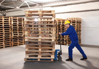 Wall Mural - Worker moving wooden pallets with manual forklift in warehouse