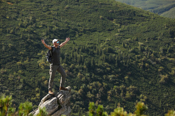 Poster - Tourist with backpack standing on rocky peak in mountains