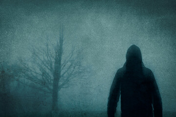 Wall Mural - A spooky concept. Of a blurred, hooded figure. Standing in the countryside. On a bleak, moody winters day. With a grainy, texture edit.