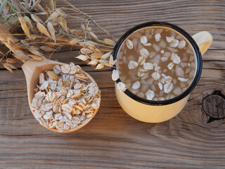 Wall Mural - Natural useful oatmeal drink in a mug, oat flakes in a spoon and spikelets of Avena sativa grain grass on a wooden background. Healthy food made from oats for vegan and vegetarian food