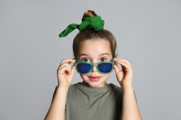 Poster - Surprised little girl with stylish bandana and sunglasses on grey background