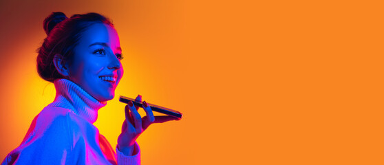 Flyer with young beautiful girl using phone isolated on orange background in neon light, filter. Concept of emotions