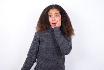 Wall Mural - Shocked teenager girl wearing grey sweater standing against wite background looks with great surprisment being very stunned, astonished with unexpected news, Facial expressions concept.