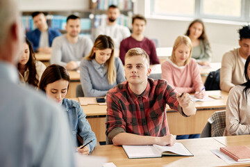 young student talking to a professor during a class at lecture hall.