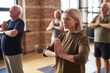 © pressmaster - Group of mature men and women keeping hands put together by chest while practicing yoga exercise in gym