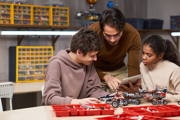 Wall Mural - Young teacher helping children to connect robots with digital tablet while they sitting at the table