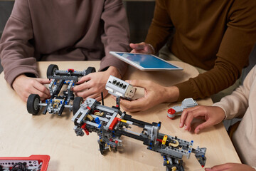 Wall Mural - Close-up of students connecting robots with digital tablet at the table during engineering lesson