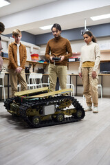 Wall Mural - Teacher controlling the big robotic machine with remote control together with his students during robotic lesson at school