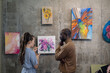© pressmaster - Young woman discussing pictures on the wall with African man while they standing in art gallery