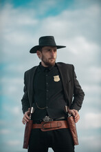 Sheriff Officer In Black Suit And Cowboy Hat. Man With Wild West Guns, Vintage Pistol Revolver And Marshal Ammunition. US Marshals, American Western Sheriff. Wild West With Cowboy.