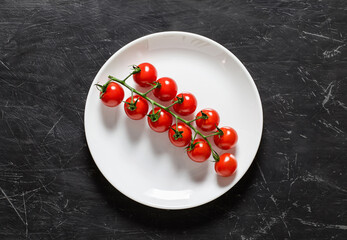 Tomatoes cherry, fresh branch on white plate, top view dark background.