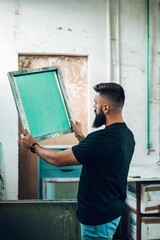 Wall Mural - Male worker holds the silkscreen frame in a printing workshop