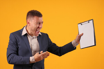 angry man in a dark suit shouts, holds a pen and a tablet for paper in his hands on a yellow background, mockup