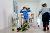 Fototapeta  - two caucasian boys making mess in the house brothers playing and mischief with bad behavior flower pot damaged on the floor naughty kids having fun at home childhood and growing up concept