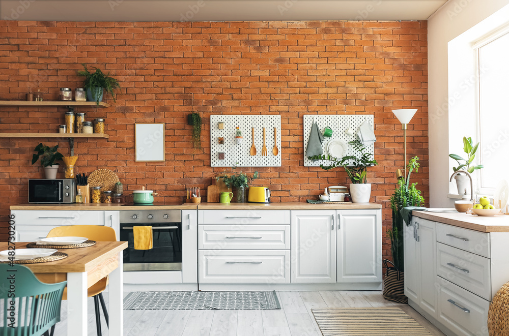 Interior of modern kitchen with white counters, pegboard and brick wall ...