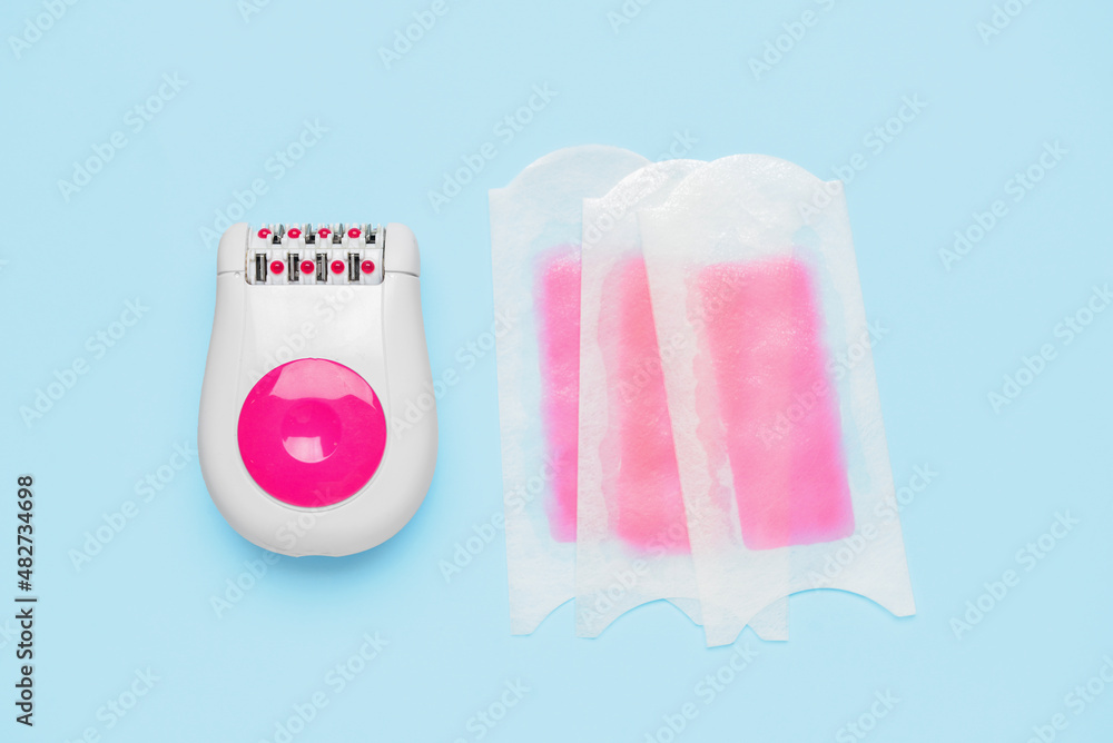 Modern epilator and wax strips on blue background