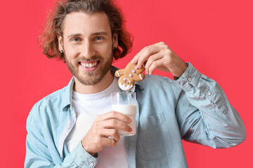 Happy young man with Christmas cookie and glass of milk on red background, closeup