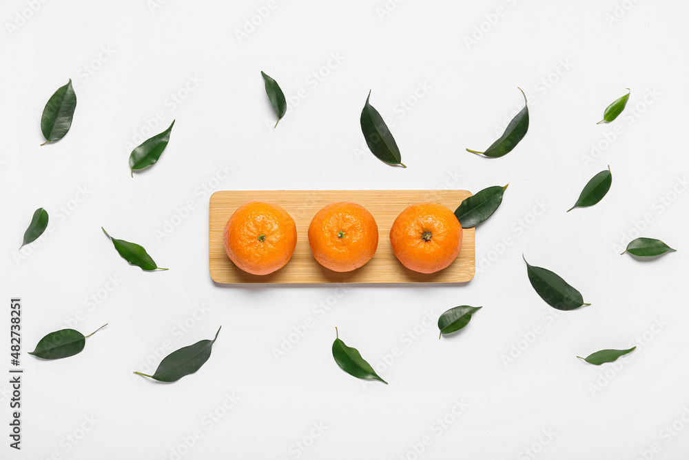 Wooden board with tangerines and leaves on white background