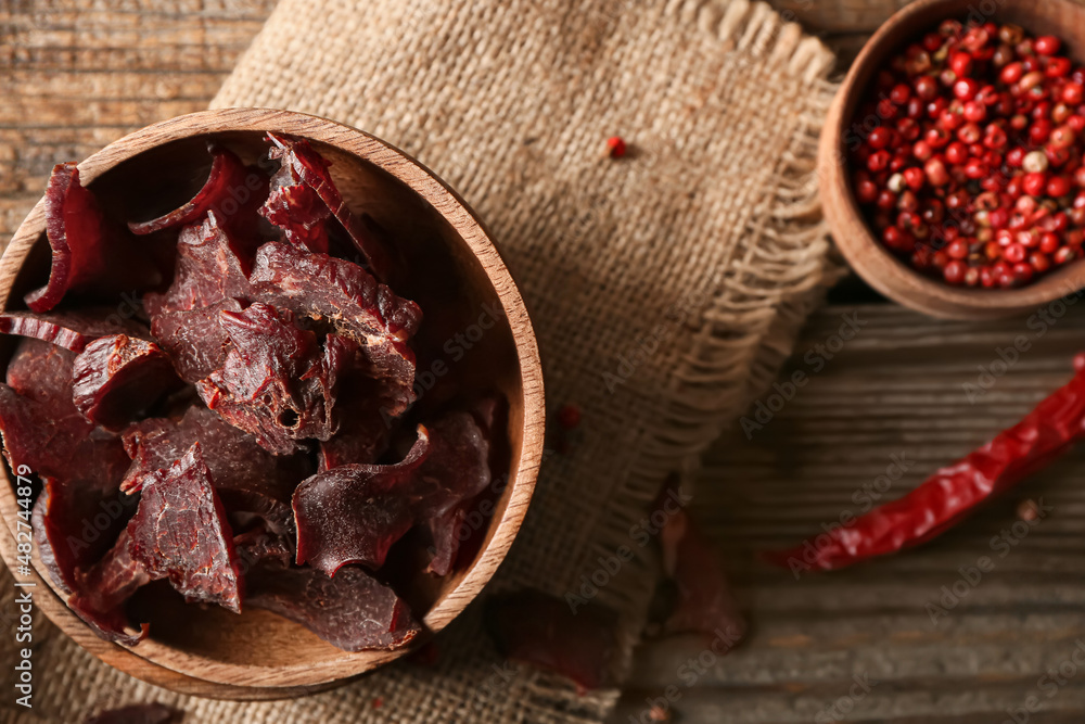 Plates with spicy beef jerky on wooden background
