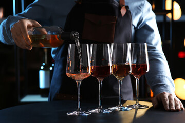 Canvas Print - Bartender pouring rose wine from bottle into glass at table indoors, closeup