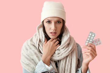 Wall Mural - Young woman with sick throat holding blisters with pills on color background