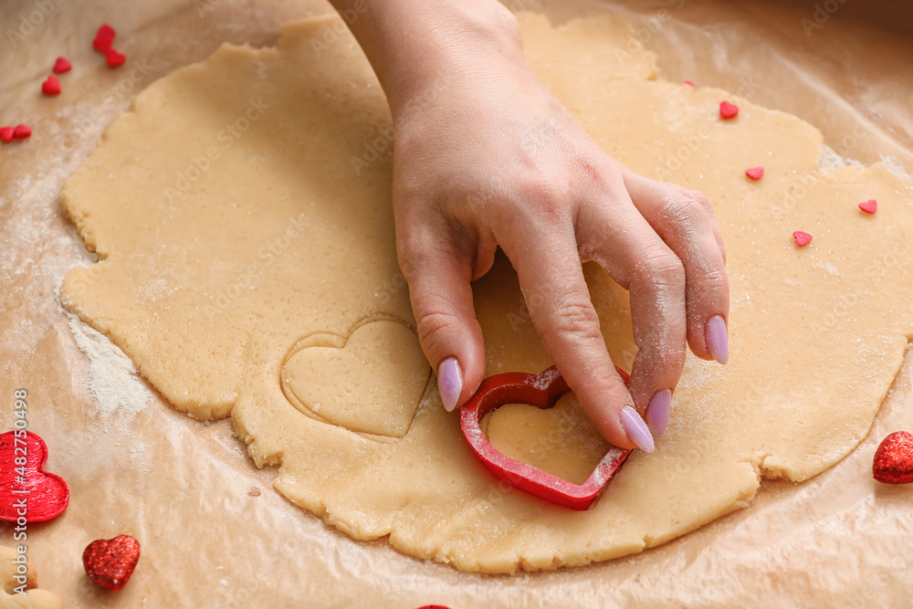 Woman preparing heart shaped cookies at table. Valentines Day celebration