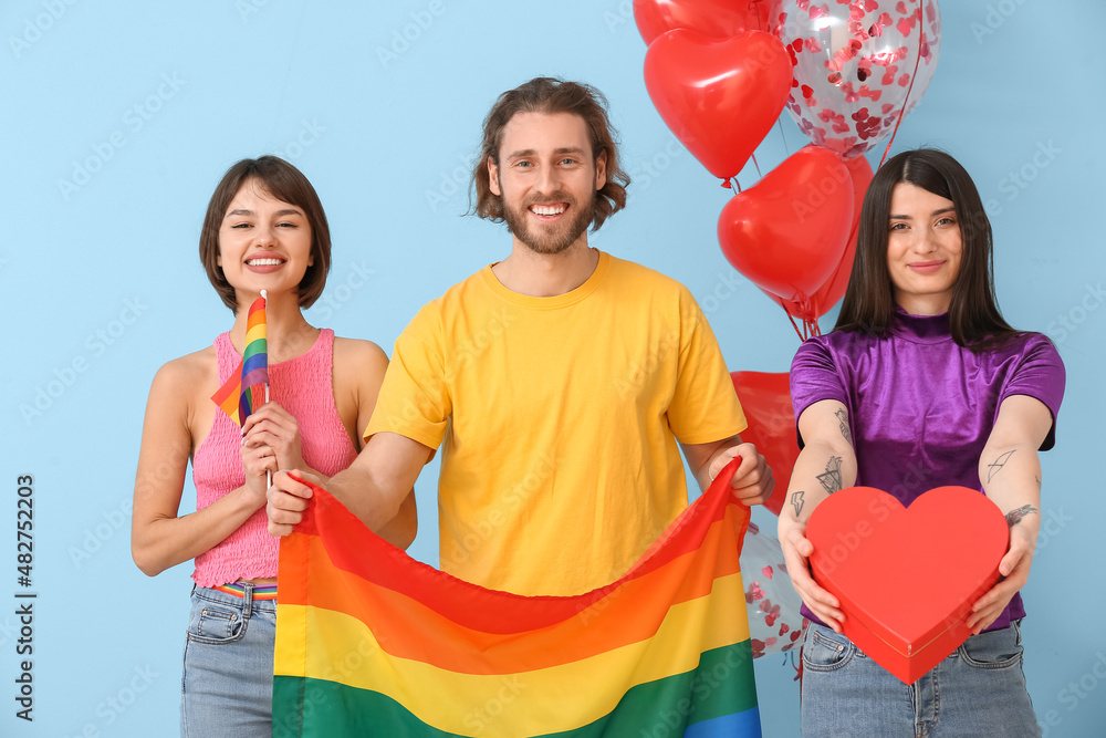 Man and two beautiful women with rainbow flags and gift on color background. Concept of polyamory and LGBT