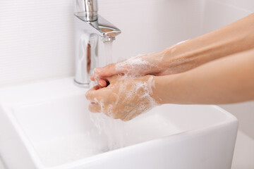 Wall Mural - Washing hands under the flowing water tap. Hygiene concept hand detail. Washing hands rubbing with soap for corona virus prevention, hygiene to stop spreading corona virus in or public wash room.