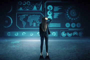 Canvas Print - Back view of attractive young european business woman standing on dark background with glowing digital hud business interface. Future, technology and innovation concept.