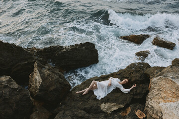 Poster - woman in a white dress lying on a stone in a white dress vacation concept