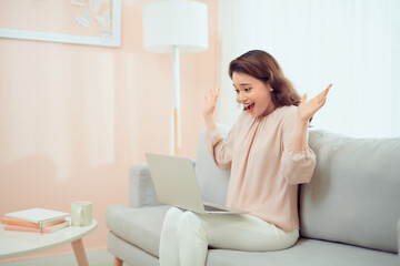 Happy smiling woman sitting at couch reading message looking at device screen using computer.