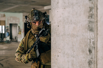 Special forces operator wearing Multicam uniform and his assault rifle HK 416 while practicing CQB combat training in the abandoned building. Coyote brown and mc gear in the urban environment.