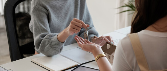 real estate agent holding house key to his client after signing contract agreement in office,concept for real estate, moving home or renting property