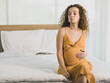 Curly hairstyle young unhappy unhealthy bad behavior Caucasian pregnancy mother in maternity long dress cloth sit on bed in bedroom holding smoking cigarette taking risk and danger to unborn child