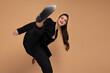 © Andrii - Businesswoman hitting with leg in camera dressed black office suit smile isolated on color background. Fight for business. Martial Art Karate pose in the studio on grey background. Kung fu style
