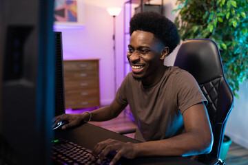 Smiling, happy boy sits in a room lit up with led colored lights, professional gamer plays computer games, laughing round, after school entertainment, virtual world