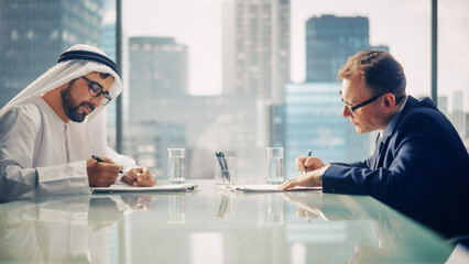 Wall Mural - Two Businessmen with Different Nationalities Sitting in Office and Signing Contract. Arab Business Partner Make with Investor Financial Deal. Saudi, Emirati, Arab Businessman Concept.