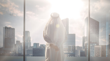 Wall Mural - Successful Muslim Businessman in Traditional White Outfit Standing in His Modern Office Looking out of the Window on Big City with Skyscrapers. Successful Saudi, Emirati, Arab Businessman Concept.