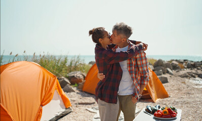 Happy tourist couple embracing and kissing, enjoying the time spending with each other. Romantic camping weekend on seashore