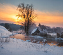House In The Village Near The River Against The Backdrop Of The Mountains On A Winter Evening At Sunset