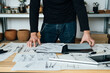 © Tijana - An Anonymous Designer Working in his Office. Unrecognizable furniture designer standing at his table with open folder, blueprints, documents, sketches and digital tablet.