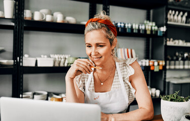 Giving my website one last look. Cropped shot of an attractive mature woman sitting alone and using her laptop in her pottery workshop.