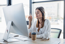 Businesswoman In Headset Looking At Computer Monitor While Pointing With Finger.