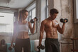 Slender young female and athletic man holding black dumbbells and doing hand exercise together in the gym