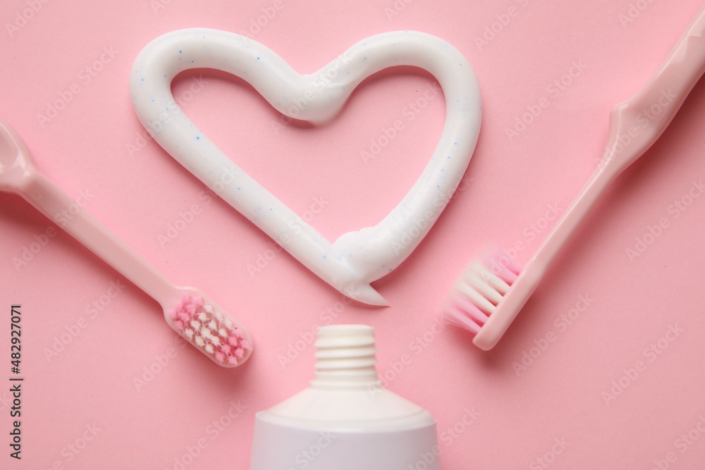 Opened tube, toothbrushes and heart drawn with toothpaste on color background