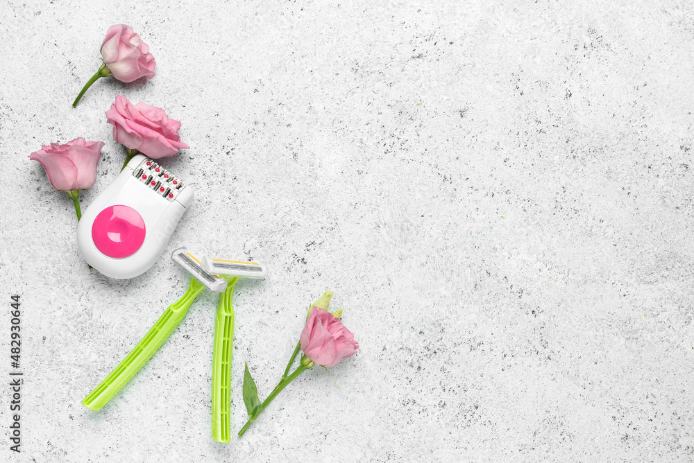 Modern epilator, flowers and razors on light grunge background
