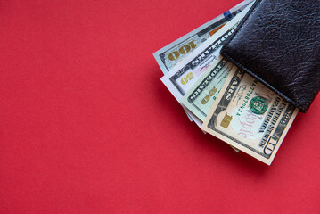 black leather wallet with dollar bills in different denominations on a red background