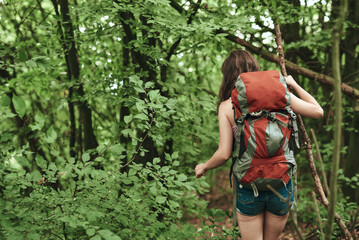 Young female hiker; woman moving through the forest, carrying large backpack, using a walking stick, finding her path in the woods