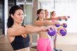 Focused active young adult woman doing workout with toning weight balls at group pilates class