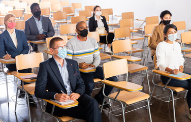 Wall Mural - Group of diverse business people wearing face masks for viral protection and keeping social distance listening to speaker at conference, the new normal